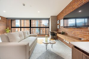 A modern living room with a sofa, a coffee table, and a TV mounted on a brick wall. - Unique loft with 1BR & sofa bed, A/C, Terrace & Rooftop Gym (Medellín)