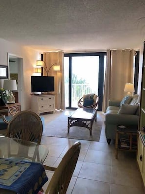 A living room with a television, a dining table, chairs, a sofa, and a balcony with curtains. - Beachfront oasis heated pool stunning views U11 (Marathon)