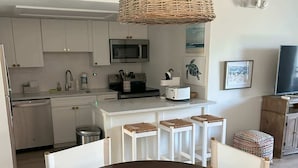 A modern kitchen with white cabinets, a microwave, and a toaster. There is a dining area with a round table and chairs. - Keys Coastal Escape Pool Beach Ocean U20 (Marathon)