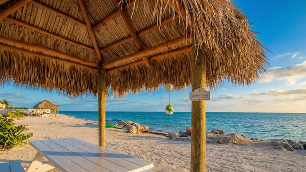 A beach with a thatched-roof structure, a sign reading 'Jolly's Beach,' and a picnic table. - Keys Coastal Escape Pool Beach Ocean U20 (Marathon)