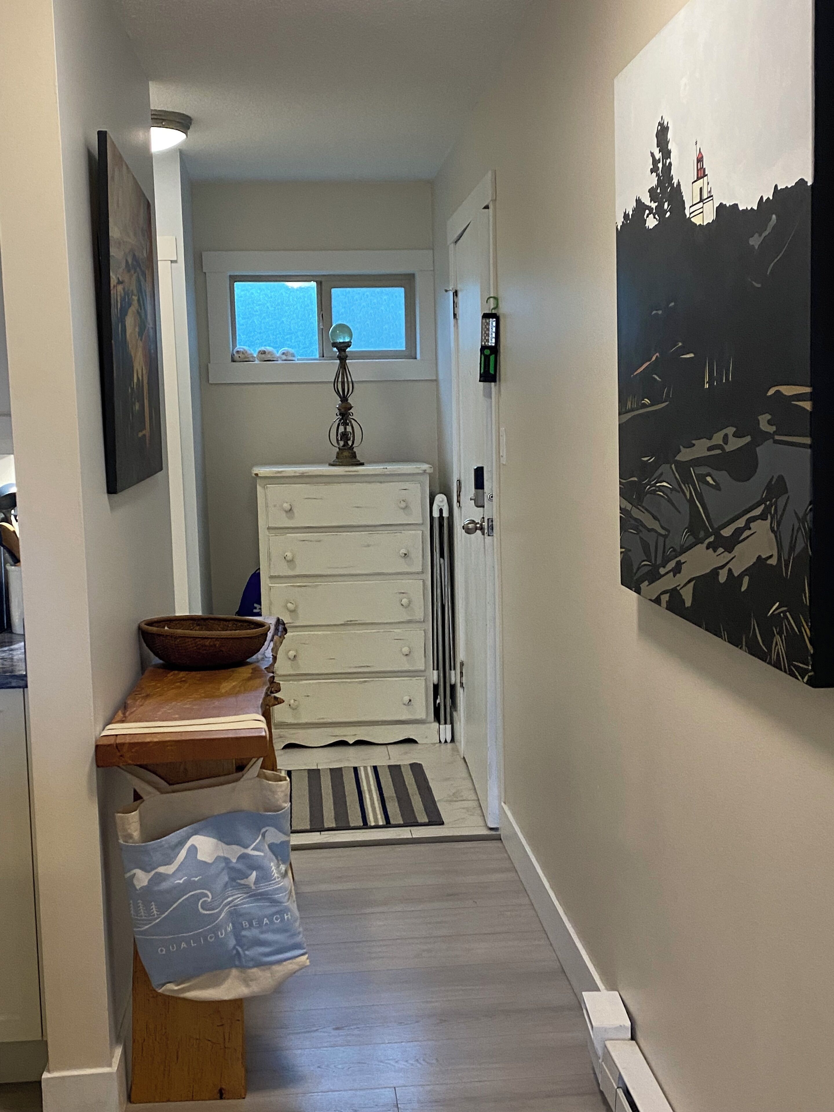 A narrow hallway with a wooden bench, a white dresser, and a painting on the wall.