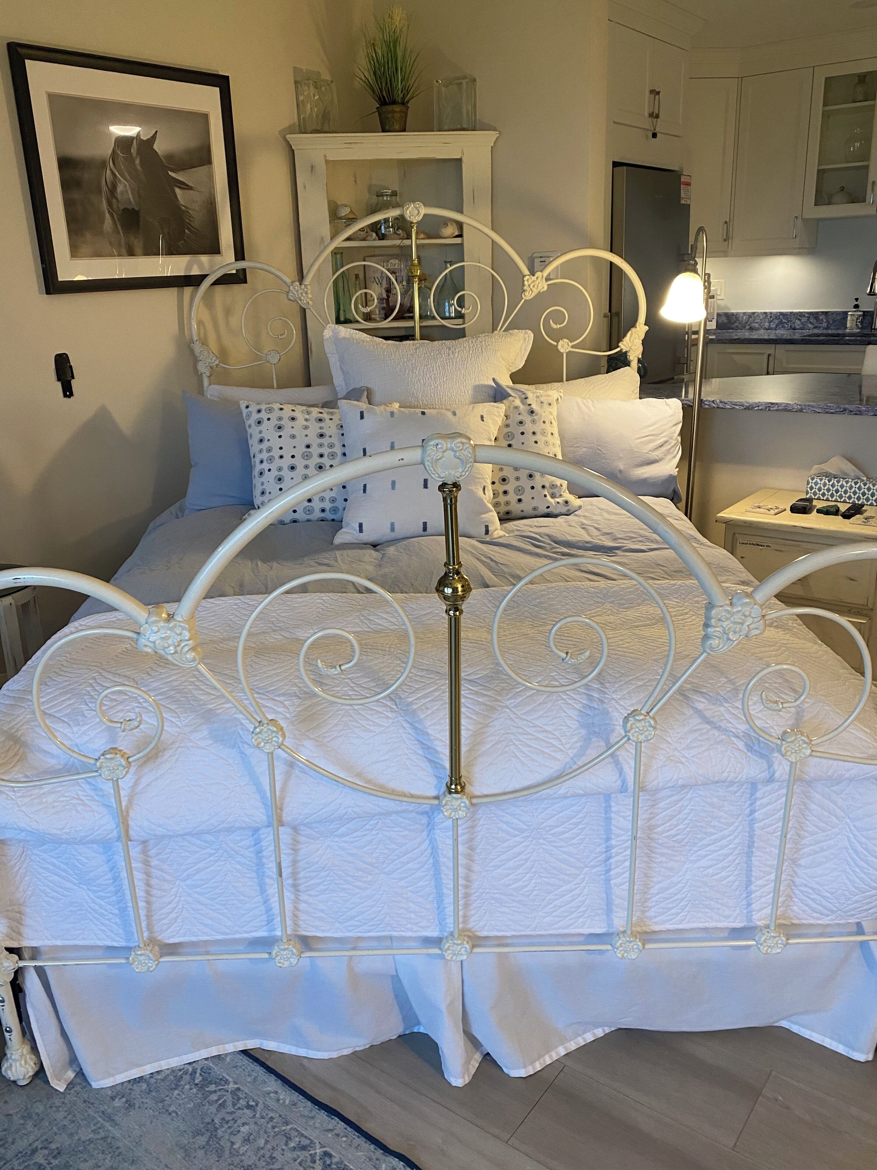 A neatly made bed with a white metal frame and a white quilted bedspread.
