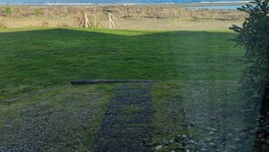 Een grasveld met een pad dat leidt naar een rotsachtig strand, een heldere lucht en verre bergen.