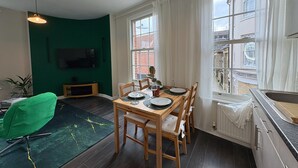 Un coin repas avec une table dressée pour quatre personnes, un fauteuil vert et un téléviseur fixé au mur.