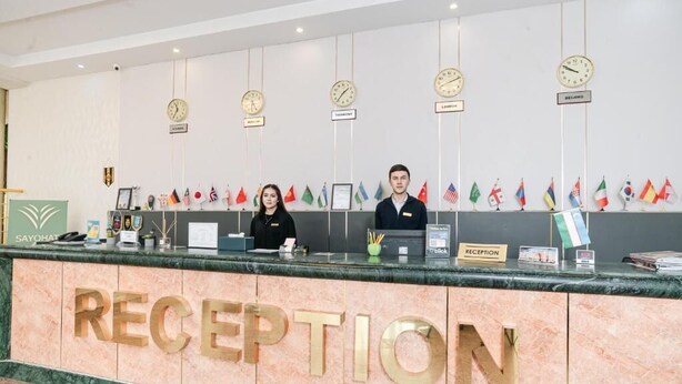Una mesa de recepción con mostrador de mármol, relojes, banderas y un cartel que dice "RECEPTION".
