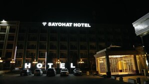 El exterior del Hotel Sayohat de noche, con señalización iluminada y coches estacionados al frente.