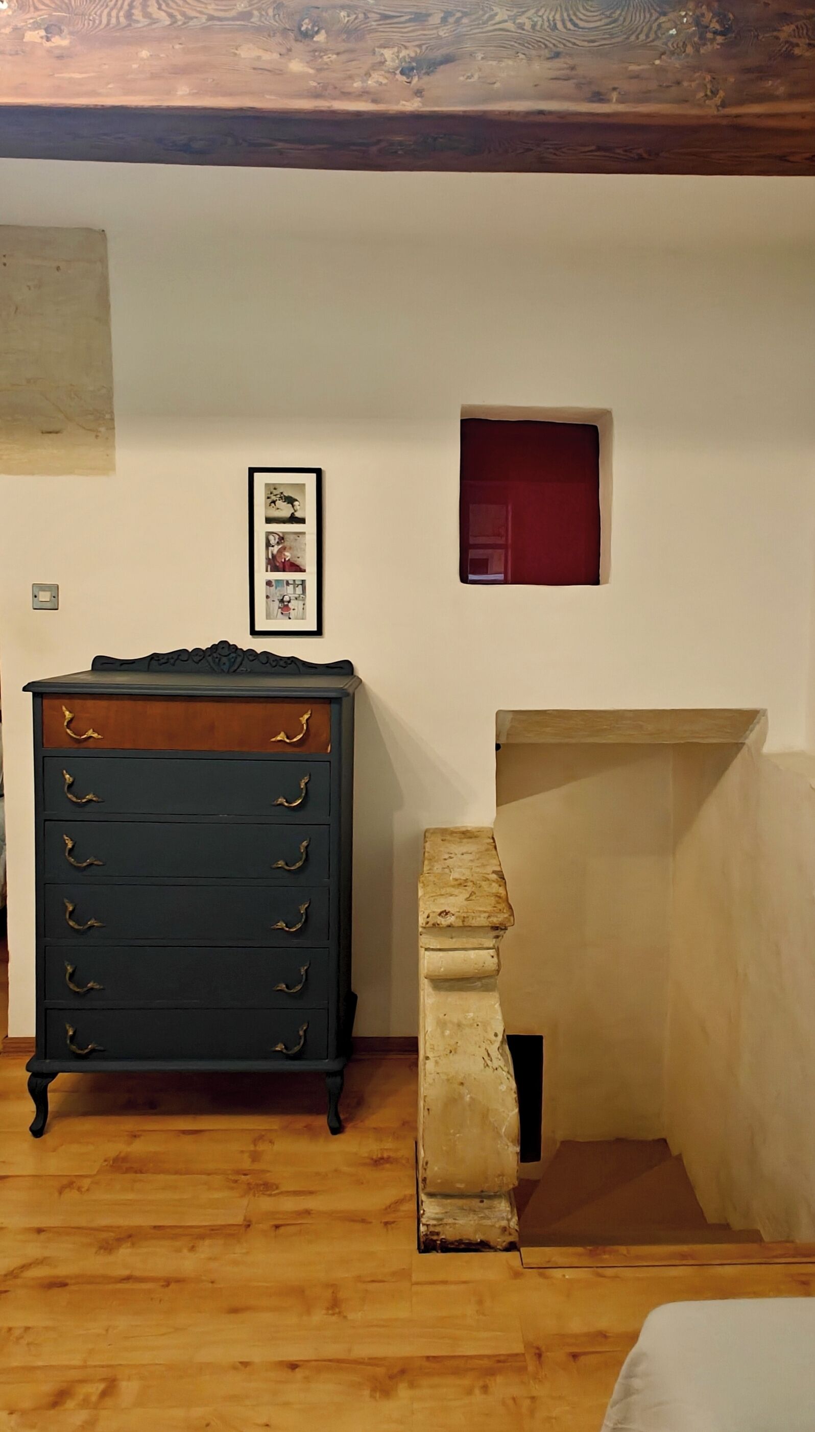 Una habitación con un aparador de madera, un pequeño cuadro enmarco y un banco de piedra.