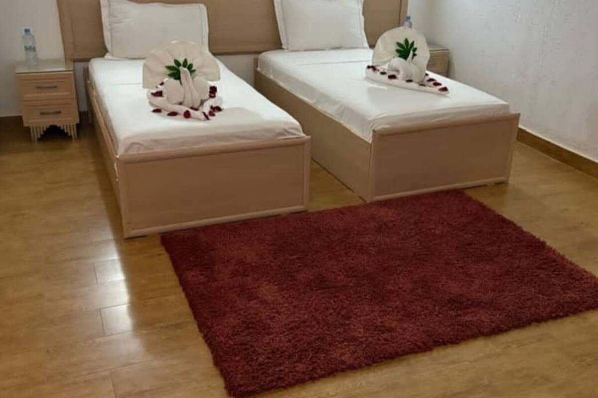 Ein Zimmer mit zwei Betten, einem roten Teppich und einem Nachttisch mit einer Wasserflasche.