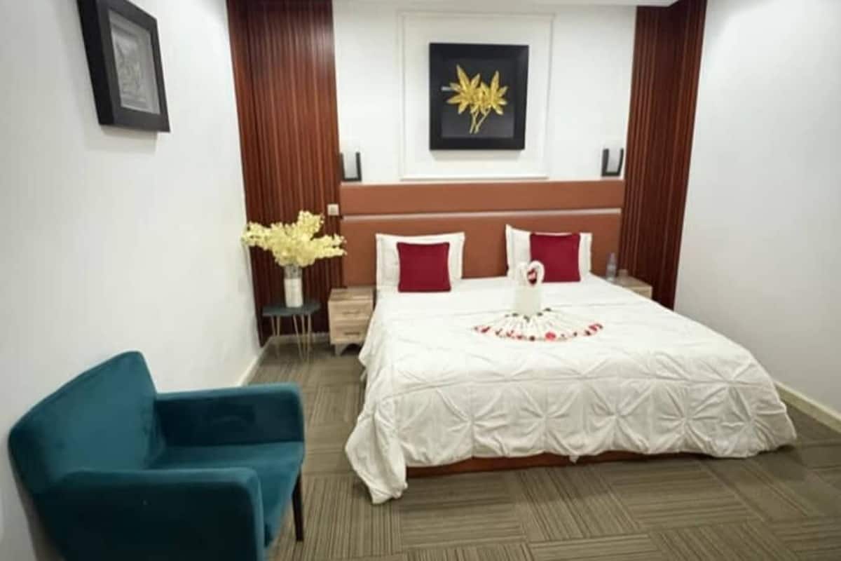 Ein Hotelzimmer mit einem Bett, einem blauen Sessel, einem kleinen Tisch mit Blumen und einem gerahmten Bild an der Wand.