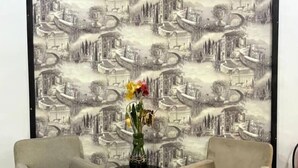 Et værelse med to lænestole, der vender mod et stort vægmaleri med et bybillede. Et lille bord med en blomstervase står placeret imellem stolene.