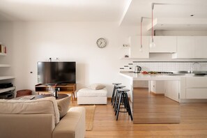 A modern living room with a flat-screen TV, a sofa, a coffee table, and a kitchen area with a sink and countertop. - Gimber Lofts 3 by Klodge - design flat with Wi-Fi (Olbia)