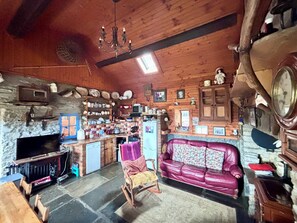 A rustic cabin interior with a stone fireplace, wooden walls, a leather sofa, and a wooden dining table.