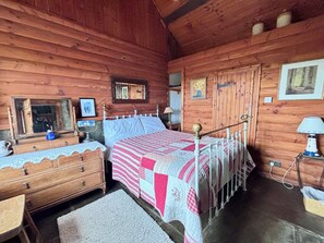 A wooden cabin bedroom with a bed, dresser, and a mirror.