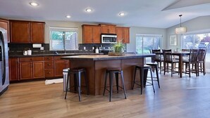 A spacious kitchen with wooden cabinets, a central island with stools, and a dining area with chairs. - Happy's Hideaway w/ Hot Tub, Sleeps 12, Downtown! (Ellensburg)