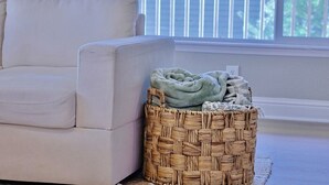 A room with a white sofa and a woven basket with a blanket and newspapers. - Happy's Hideaway w/ Hot Tub, Sleeps 12, Downtown! (Ellensburg)