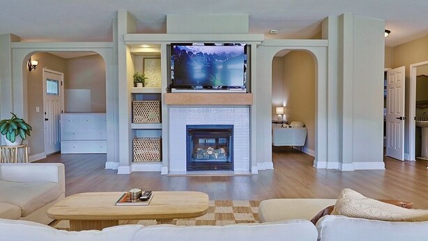A spacious living room with a fireplace, a flat-screen TV mounted above it, and a cozy seating area with a coffee table. - Happy's Hideaway w/ Hot Tub, Sleeps 12, Downtown! (Ellensburg)