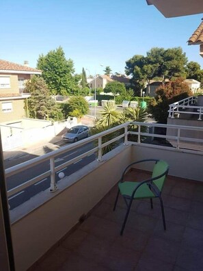 Ein Balkon mit Stuhl, Geländer und Blick auf eine Straße mit Autos und Häusern.