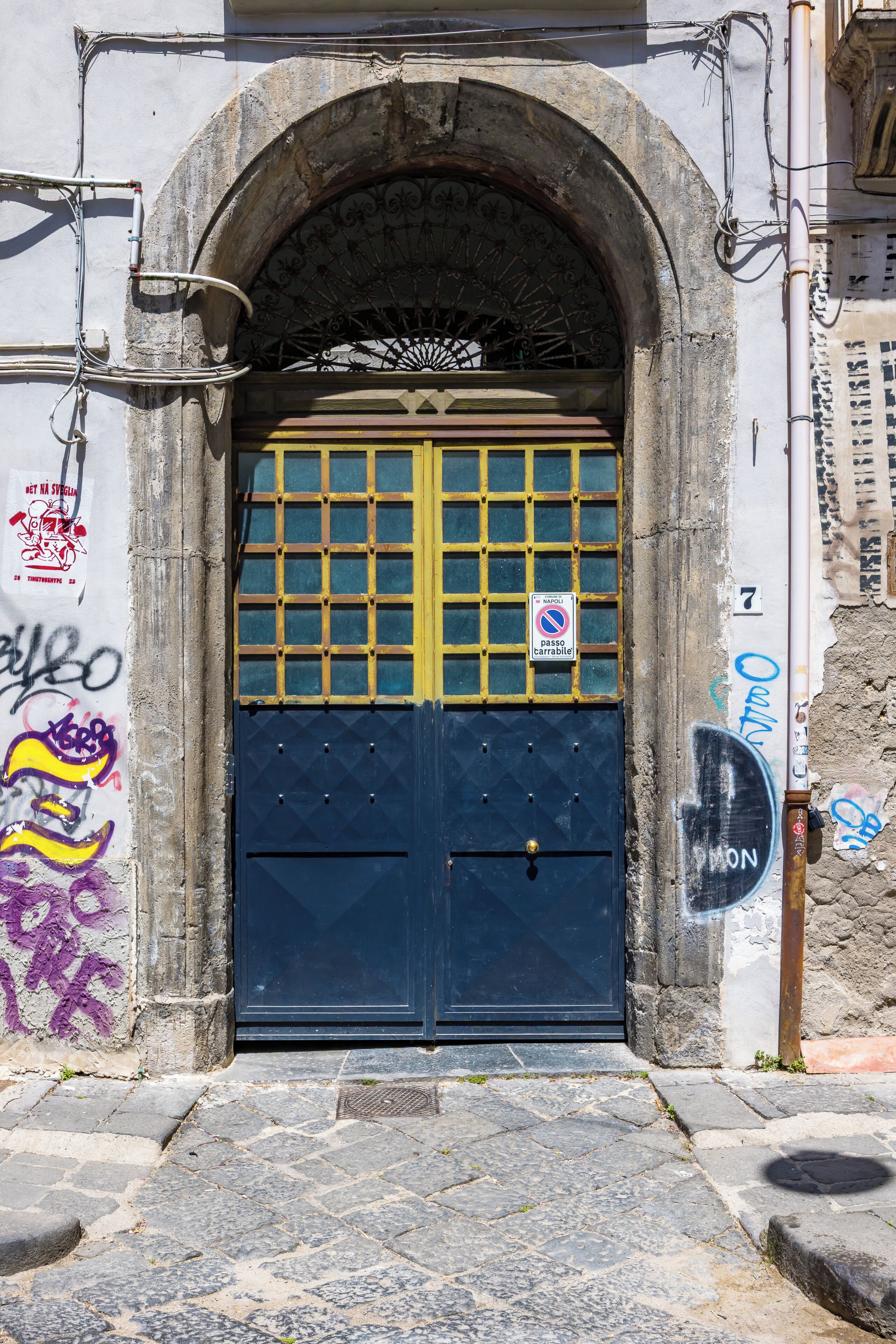 Una porta de blau fosc amb un dibuix de reixa, un petit cartell a dalt i grafits al mur.