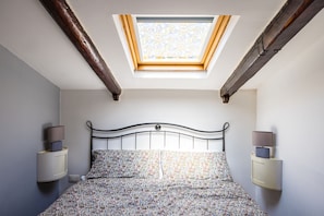 A bedroom with a skylight, a bed with floral bedding, and bedside lamps. - Alessio's House by NapoliApartments (Naples)