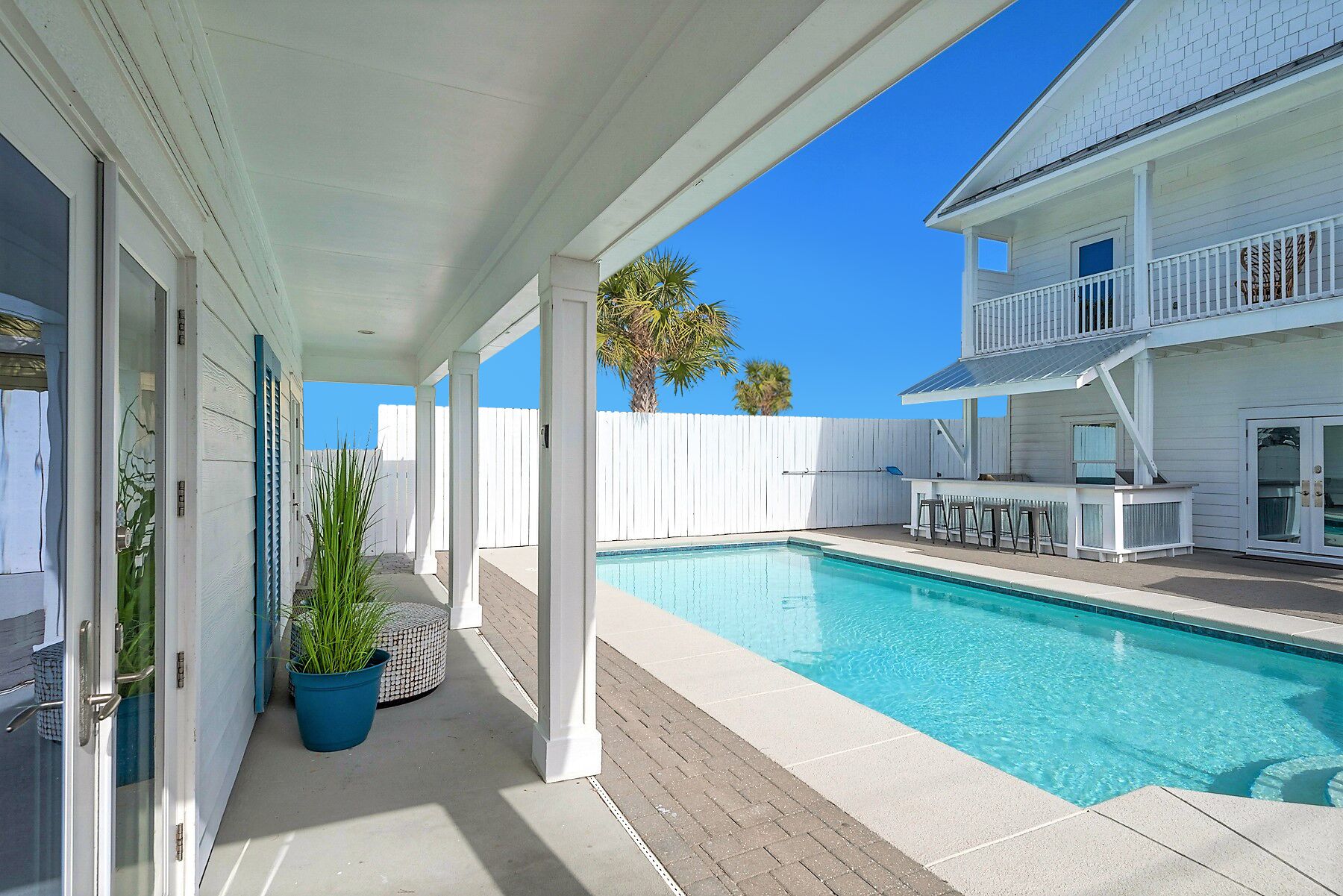 A pool area with a covered patio, a white fence, and a two-story building with a balcony.