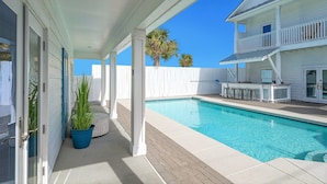 A pool area with a covered patio, a white fence, and a two-story building with a balcony. - Epic! Ocean views! Sleeps 20! Pool! Golf cart! (Destin)