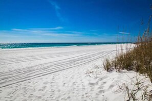 A sandy beach with footprints leading to the water, and tall grasses on the right. - Epic! Ocean views! Sleeps 20! Pool! Golf cart! (Destin)