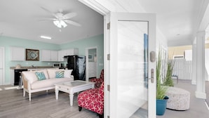 A modern living room with a white sofa, a red ottoman, and a glass coffee table. A black refrigerator is visible in the background. - Epic! Ocean views! Sleeps 20! Pool! Golf cart! (Destin)