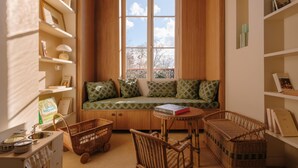 A cozy room with a wooden bench, wicker furniture, and shelves with books and decorative items. - RIVE Side House    . (Muids)