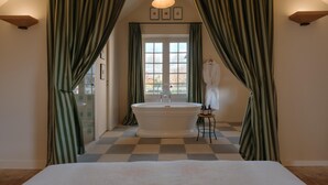A bathroom with a freestanding bathtub, a small stool, and a window with curtains. - RIVE Side House    . (Muids)