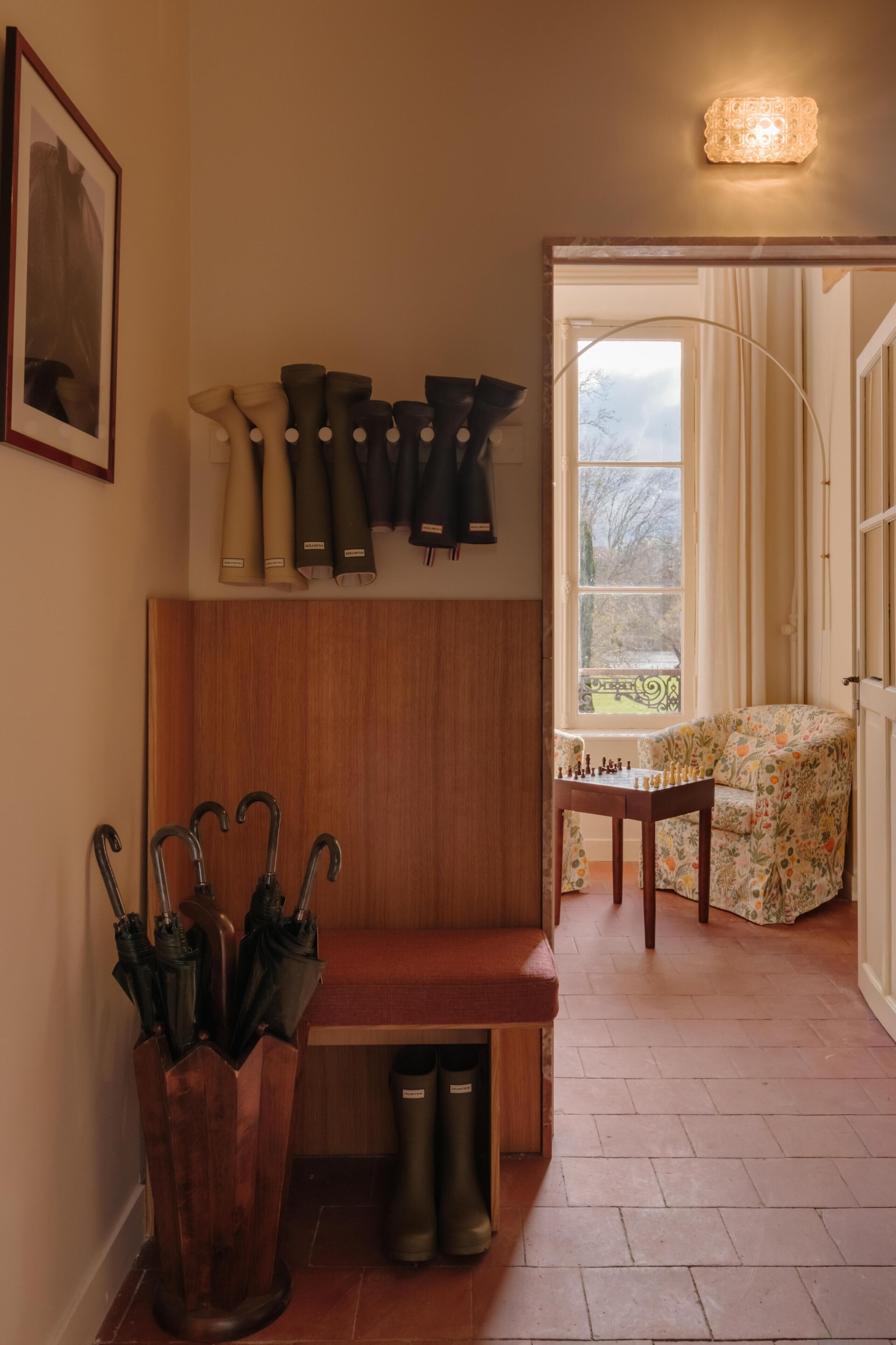 A wooden bench, a chessboard, a window with curtains, and a wall-mounted umbrella rack.