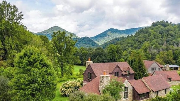A cluster of traditional stone and wooden houses surrounded by lush greenery and mountains in the background. - AHMA Cottage 2 (Canton)