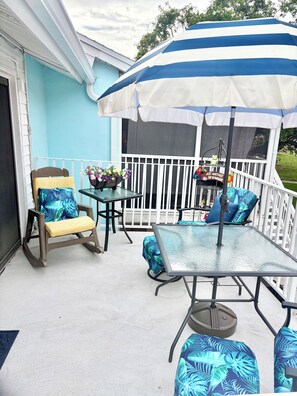 A covered outdoor patio with a table and chairs, a small table with flowers, and a decorative item on a stand. - Gorgeous 1 BR top floor + Private Beach + pools + hot tub Washer Dryer + Balcony (St. Petersburg)