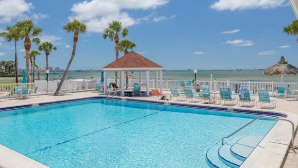 A swimming pool with lounge chairs and a gazebo, overlooking a beach. - Gorgeous 1 BR top floor + Private Beach + pools + hot tub Washer Dryer + Balcony (St. Petersburg)