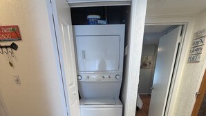 A laundry room with a front-loading washer and dryer, a door leading to another room, and a sign on the wall. - Gorgeous 1 BR top floor + Private Beach + pools + hot tub Washer Dryer + Balcony (St. Petersburg)