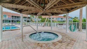 A covered outdoor area with a hot tub, pool, and lounge chairs.