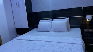 A hotel room with a large bed, white bedding, a black headboard, a wardrobe, and a nightstand with a lamp.