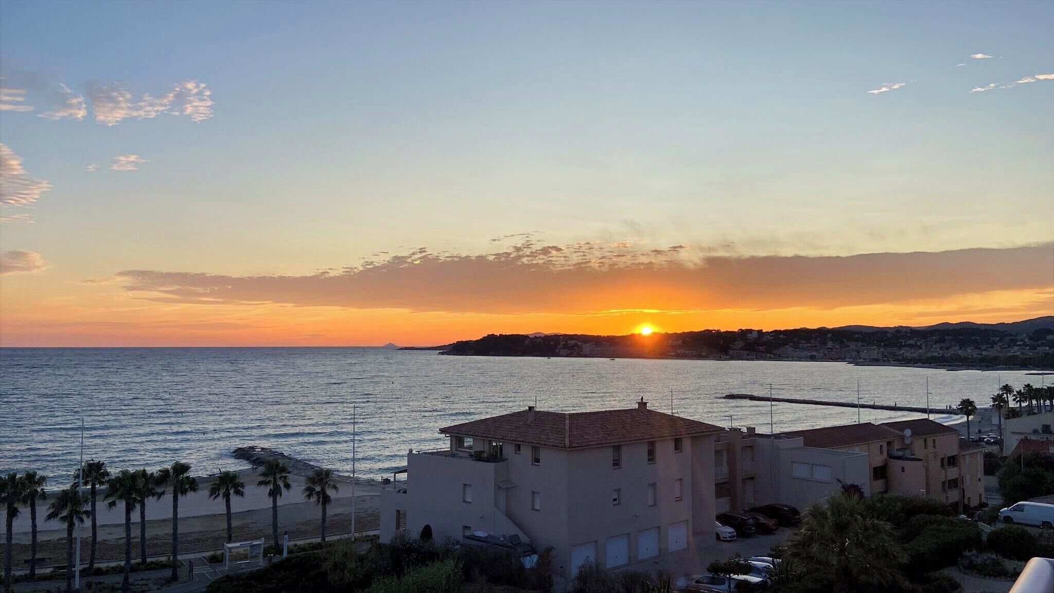 A coastal sunset view with buildings and a pier.