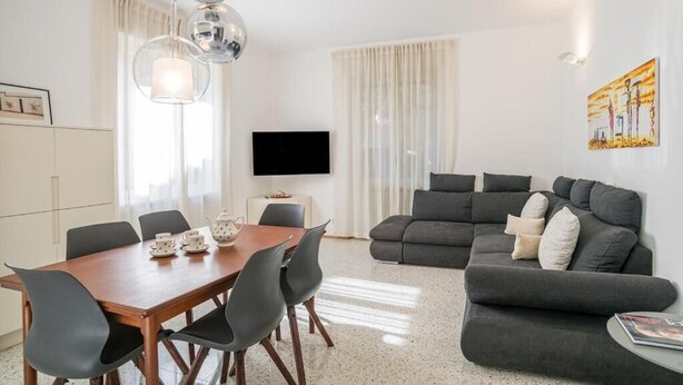 A modern living room with a dark grey sofa, a wooden dining table with chairs, a flat-screen TV, and a painting on the wall. - Central Cernobbio - Modern Apartment (Cernobbio)