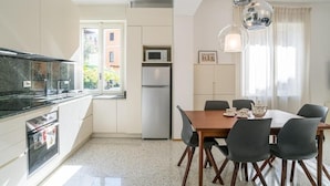 A modern kitchen with a dining area, featuring a large window, stainless steel appliances, and a chandelier. - Central Cernobbio - Modern Apartment (Cernobbio)