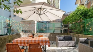 An outdoor patio with a table and chairs, a large umbrella, and wicker furniture. - Central Cernobbio - Modern Apartment (Cernobbio)