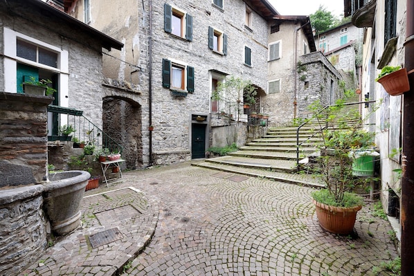 A cobblestone courtyard with stone buildings, a staircase, and potted plants.