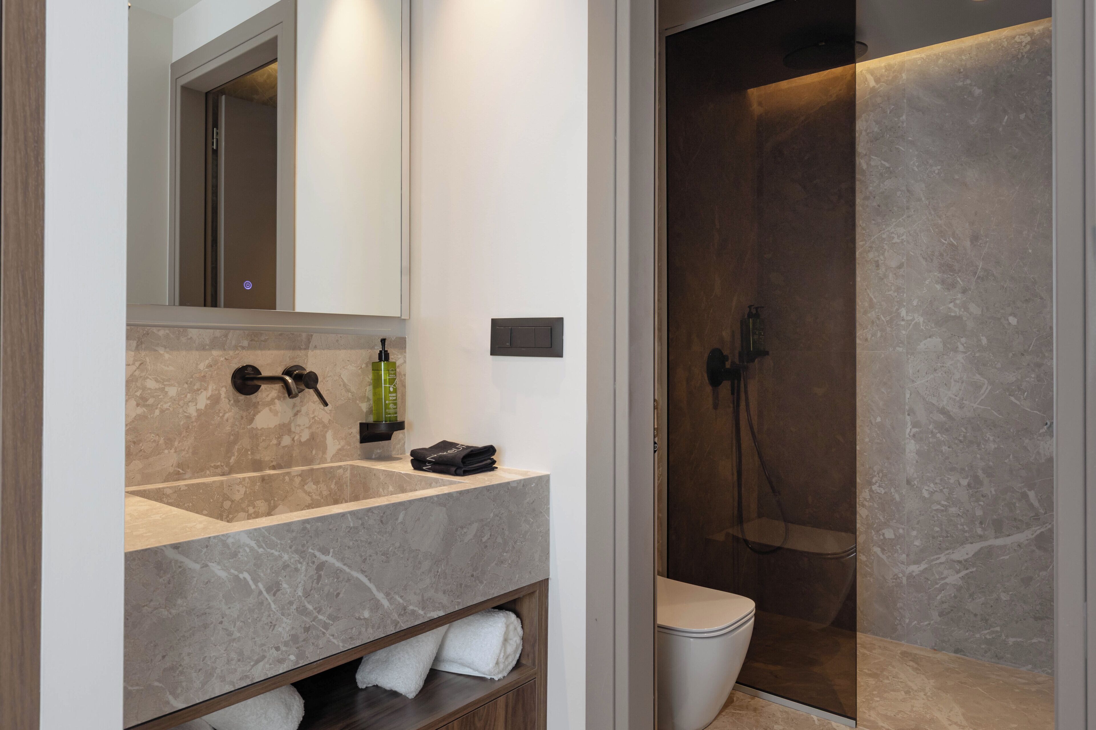 Une salle de bain moderne avec un lavabo en marbre, un miroir, un porte-serviettes et une douche à l’italienne.