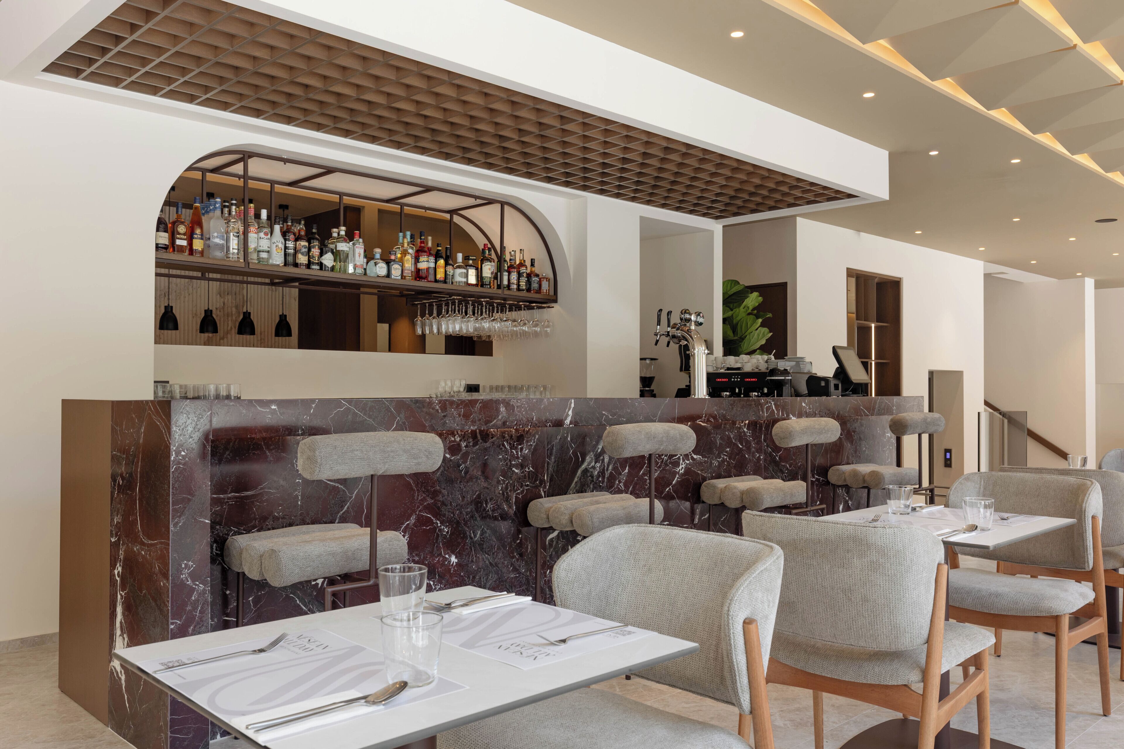 Un espace bar moderne avec un comptoir en marbre, des sièges et un assortiment de bouteilles et de verres.