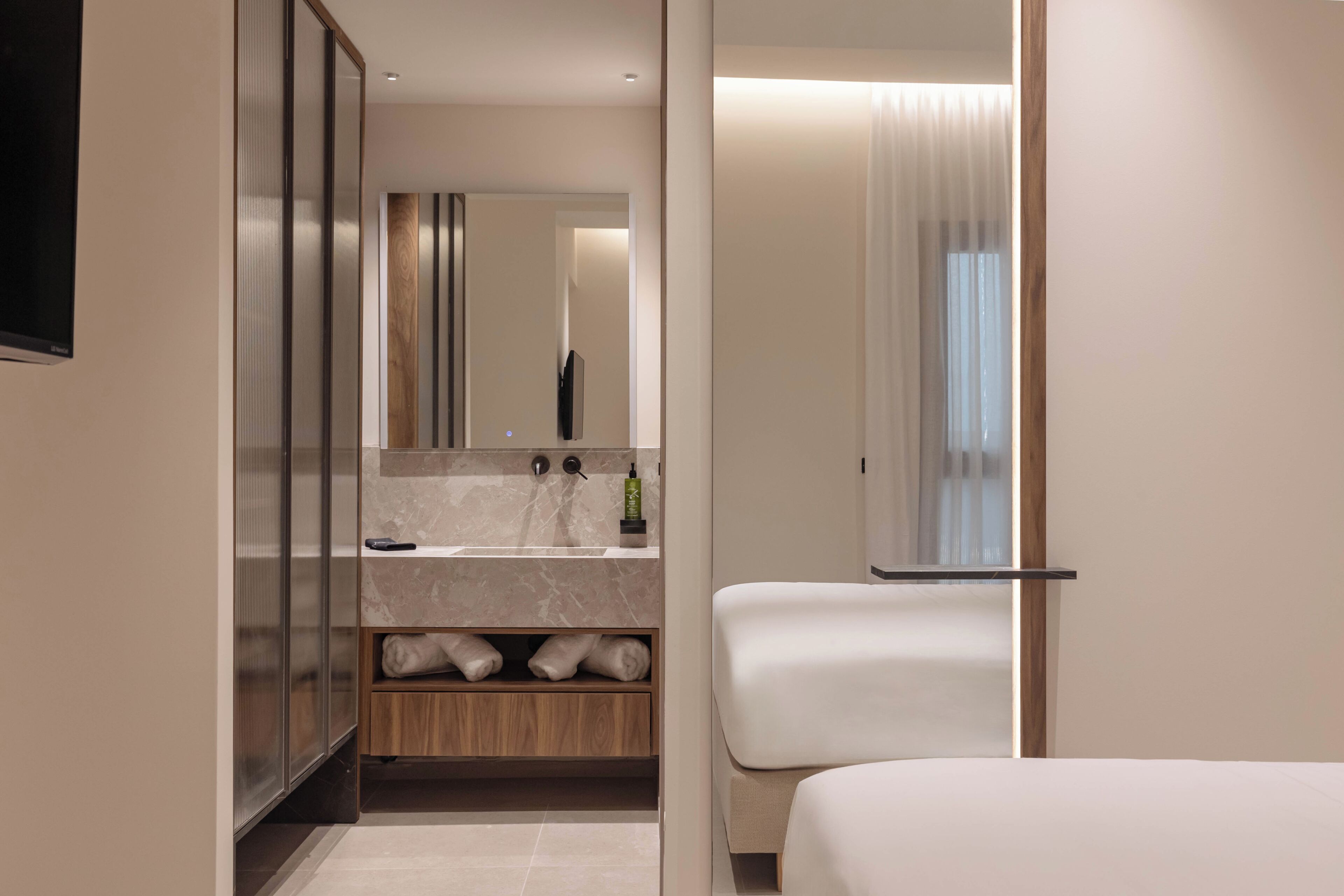 A modern hotel room with a large bed, a built-in vanity with a mirror, and a shower area.