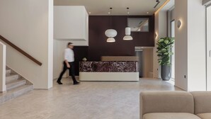 A modern lobby with a reception desk, a staircase, and a large potted plant. - Nesean Plaza Hotel (Heraklion)