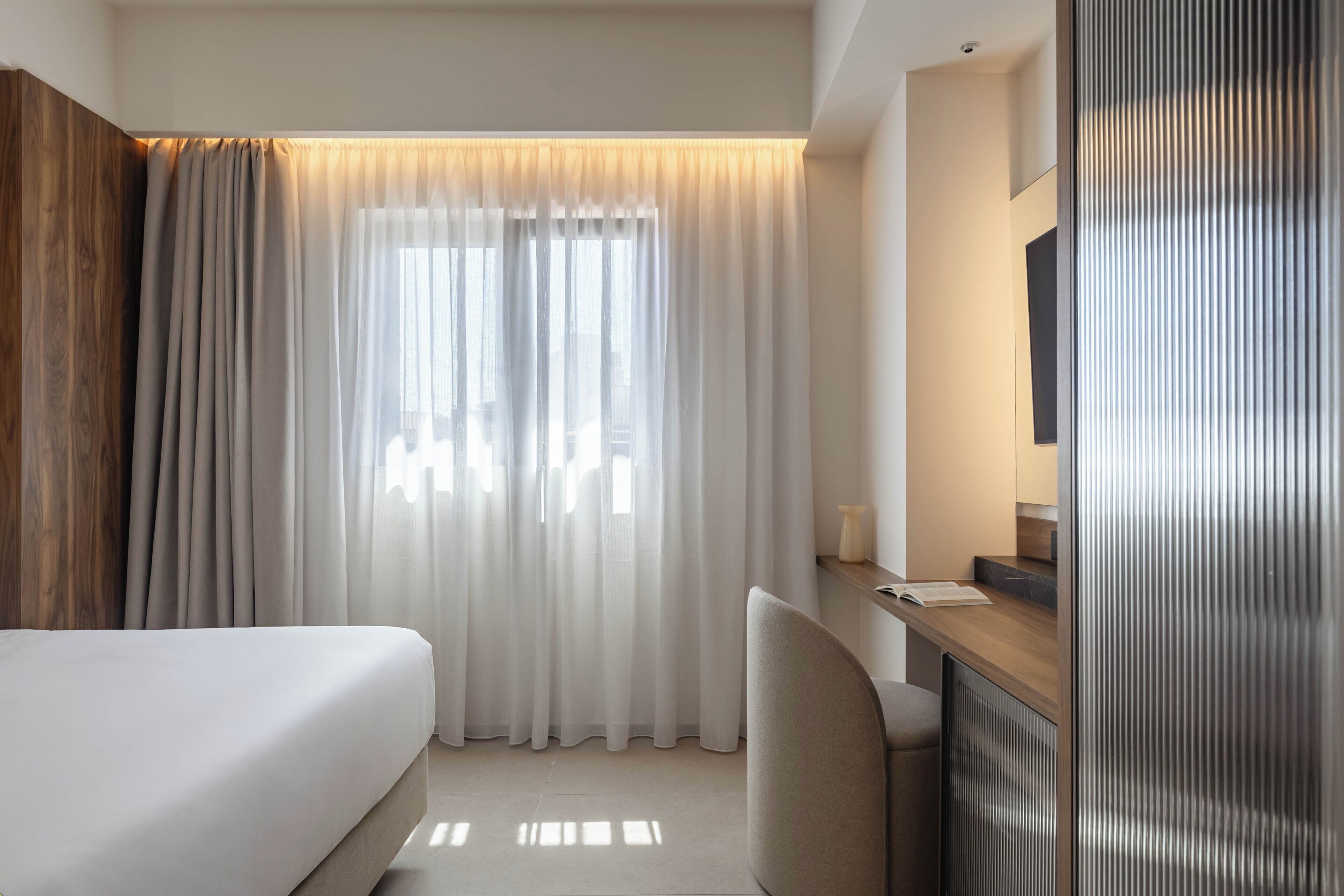 A hotel room with a bed, a desk, a chair, and a large window with curtains.