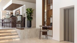 A modern interior with a marble staircase, a potted plant, a wooden bookshelf, and a closed door. - Nesean Plaza Hotel (Heraklion)