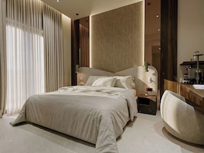 A modern bedroom with a large bed, bedside tables, a chair, and a desk with a lamp. - Nesean Plaza Hotel (Heraklion)