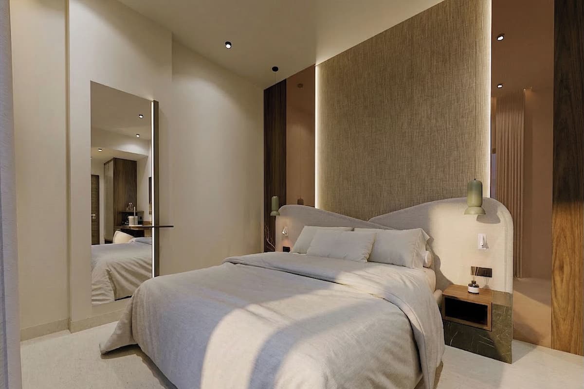 A modern hotel room with a large bed, a bedside table, a mirror, and a wall-mounted light fixture.