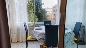 Ein Essbereich mit einem für vier Personen gedecktem Tisch, Stühle mit gelben Kissen und Blick auf Gebäude durch ein Fenster.